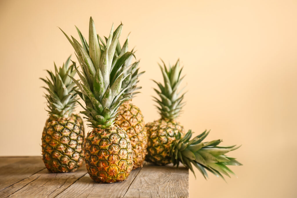 Ripe pineapples on wooden table against color background