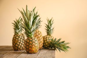 Ripe pineapples on wooden table against color background